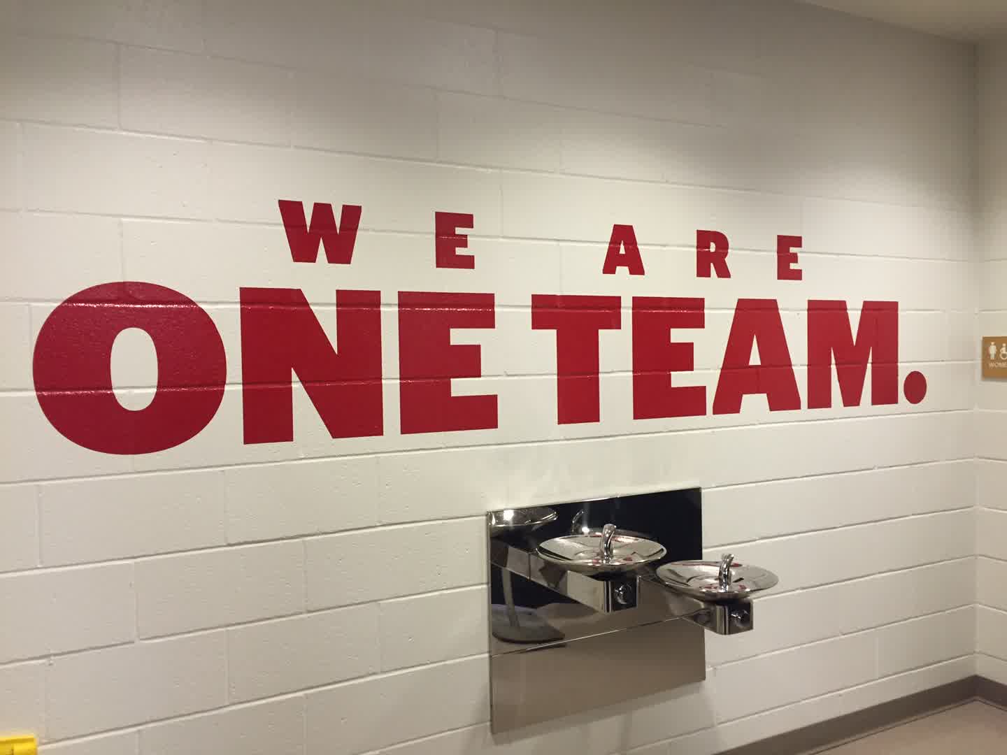 A venue wall carries a large one-team message.